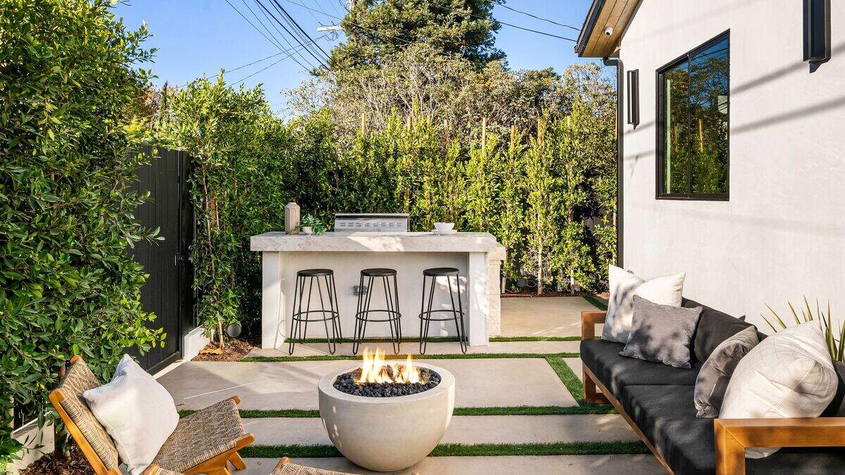 Backyard design is trending towards multiple zones called micro-rooms. Modern outdoor patio with fire pit, seating, and greenery, perfect for relaxation and gatherings.